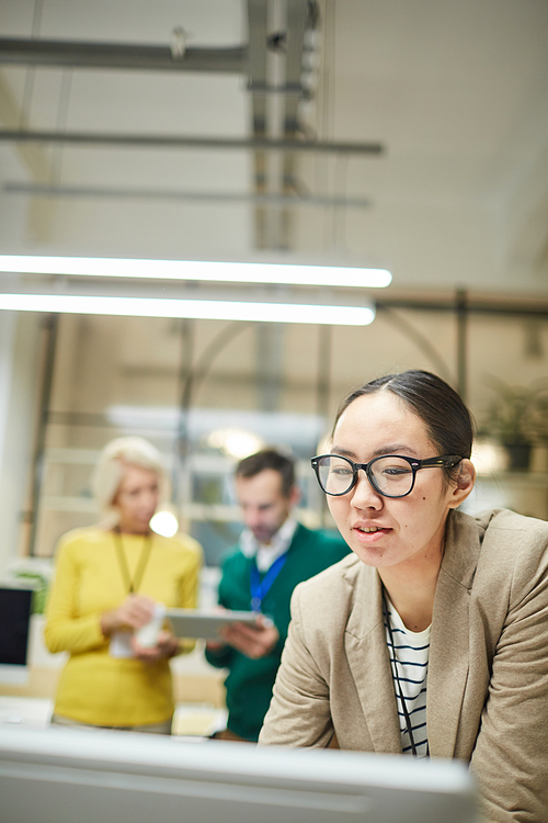 Busy female analyst in glasses standing in modern office and using computer while analyzing information