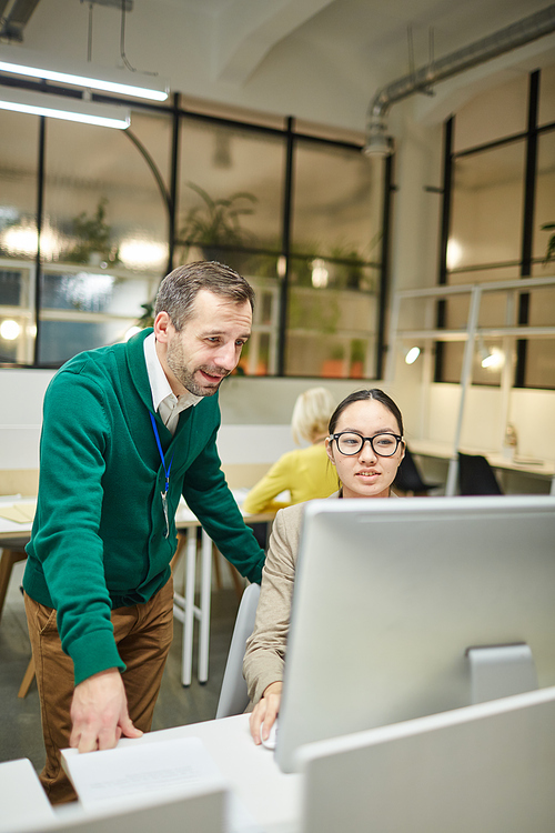 Confident handsome designer in glasses sitting at table and showing graphic design to manager in modern office