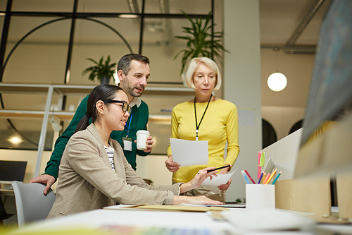 Thoughtful team of marketing specialists sitting in modern office and discussing data on laptop together