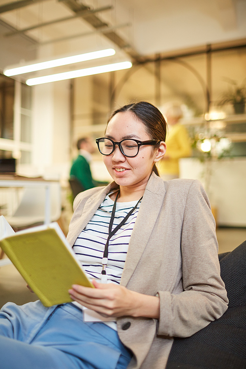 Positive attractive young Asian woman in jacket sitting in bean bag and checking timetable in personal organizer