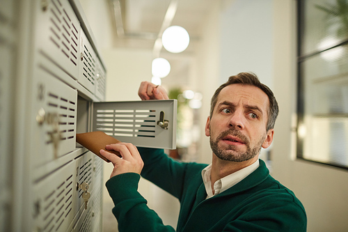 Serious frightened man with stubble hiding purse in deposit box and looking around