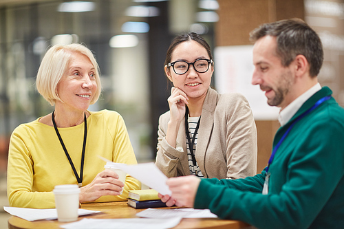 Group of positive multi-ethnic colleagues sitting at table and examining papers together