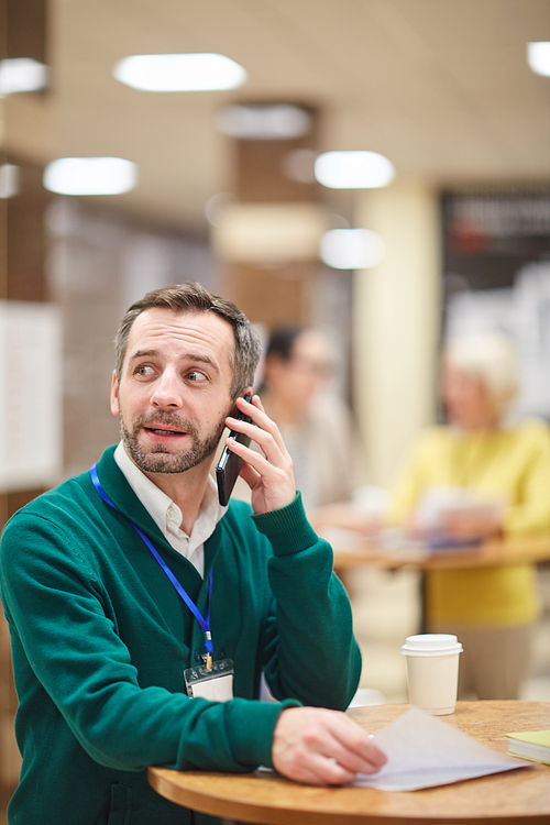 Conference participant sitting at table during coffee break, working with documents and talking on phone