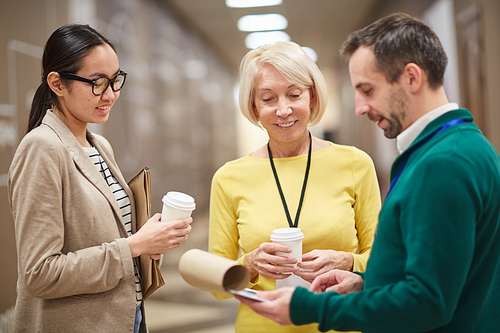 Smiling business people drinking coffee and discussing document with schedule of conference