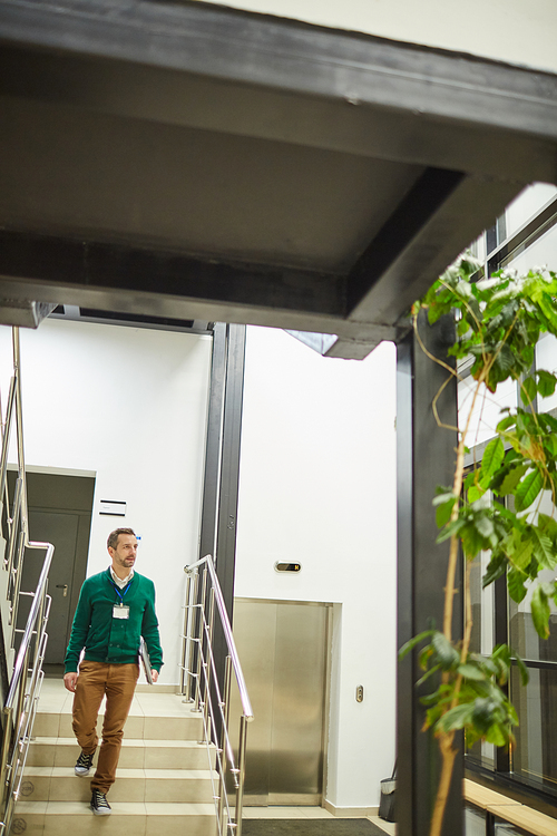 Conference planner with badge on his neck walking down the stairs in office hall