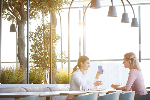 Enterprising young woman in white blouse showing new business app to colleague while they having lunch in restaurant