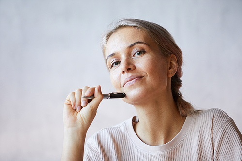 Portrait of content creative young lady in sweater leaning chin on pen and thinking of own business