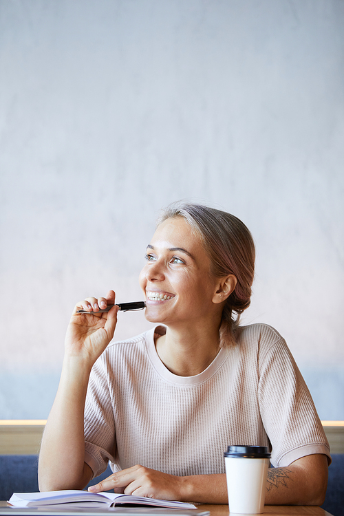 Dreamy excited freelance journalist with ash-colored hair sitting at table and thinking of new ideas for article