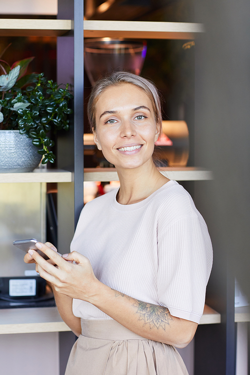 Portrait of cheerful beautiful young woman with tattoo on arm using modern phone while texting message