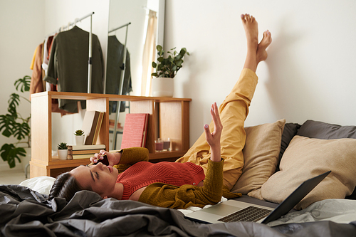 Young woman lying with feet on wall and discussing last news by phone at home