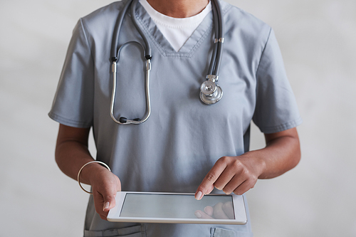 Medium section studio shot of unrecognizable female doctor wearing gray uniform using digital tablet