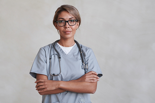 Horizontal medium studio portrait of modern female doctor wearing eyeglasses standing with arms crossed looking at camera