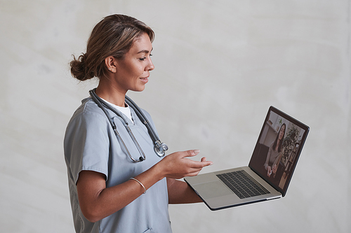 Horizontal medium studio portrait of modern female doctor holding laptop talking to patient on video call
