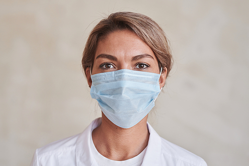 Horizontal close-up portrait of modern young adult female doctor wearing protective mask looking at camera