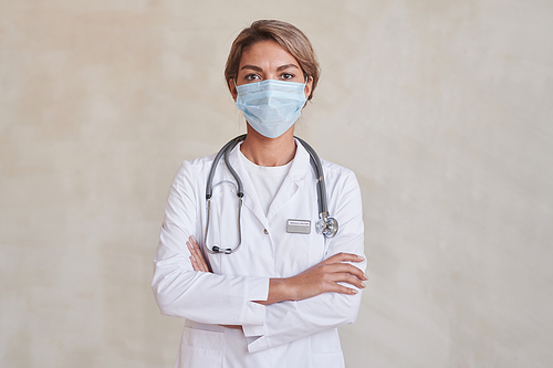 Horizontal medium portrait of modern young adult medical specialist wearing protective mask standing with arms crossed looking at camera
