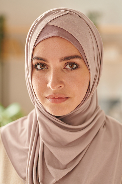 Vertical head and shoulders close-up portrait shot of attractive Muslim woman wearing pale pink hijab looking at camera