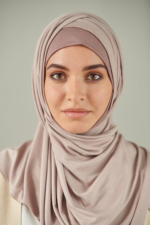 Vertical head and shoulders portrait of beautiful young woman wearing pale pink hijab looking at camera