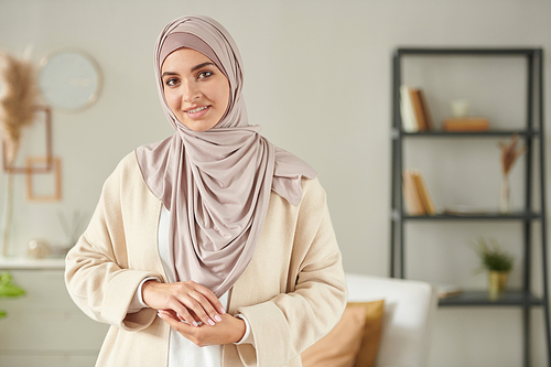 Horizontal medium portrait of young woman wearing casual outfit with pastel pink headscarf smiling at camera