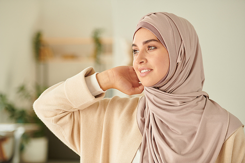 Beautiful young Muslim female model fixing her hijab and looking away, horizontal chest up portrait shot