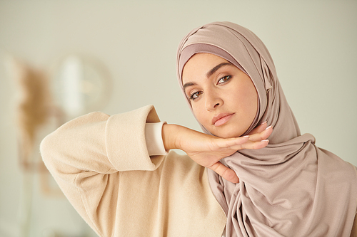 Sensual Middle Eastern woman wearing hijab posing on camera with her hand under chin, copy space