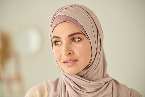 Head and shoulders close-up portrait of young adult Muslim woman wearing pale pink hijab looking away