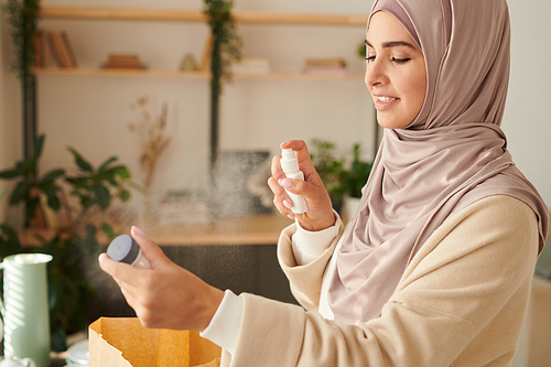 Horizontal medium portrait of modern young Muslim woman in hijab disinfecting things delivered to her during quarantine time