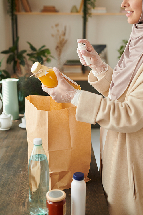 Vertical shot of modern young Muslim woman wearing protective gloves disinfecting things delivered to her during quarantine time