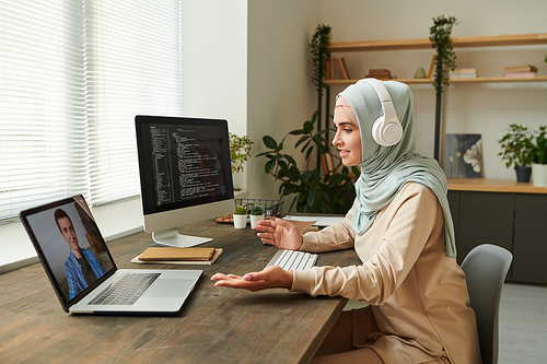 Remote IT specialist wearing headphones discussing new software development problems with her colleague