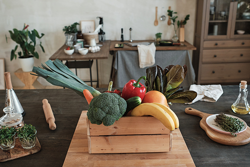 Ripe vegetable and fruit ingredients for dinner in wooden box placed on table with herbs and oil