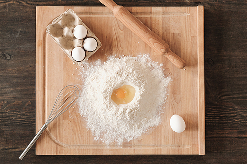 Directly above view of wooden board with flour, eggs, whisk and rolling pin on kitchen counter