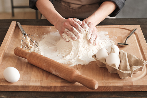 Close-up of unrecognizable woman touching hill of flour while kneading dough with hands