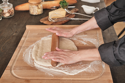 Close-up of unrecognizable woman in black shirt using rolling pin while rolling dough on wooden board