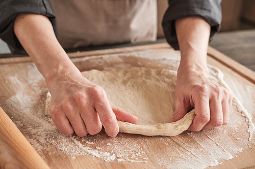 Close-up of unrecognizable woman spreading dough onto wooden board while preparing it for cutting out
