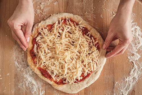 High angle view of female hands adjusting shape of pizza dough while preparing pizza for baking