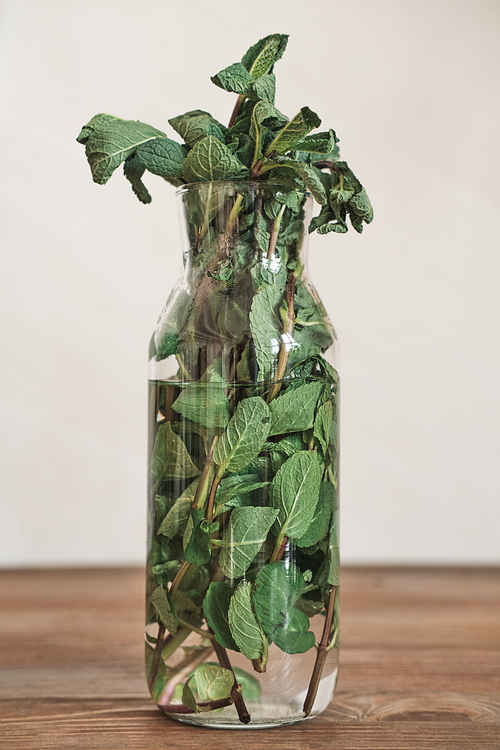 Close-up of mint leaves in vase with water placed on wooden table, refreshing ingredient for dishes