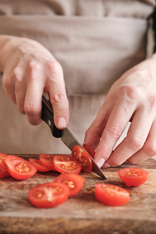Close-up of unrecognizable woman cutting cherry tomato with knife on wooden board