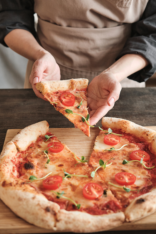 Female hands taking hot pizza slice with tomato and pea leaves while eating it after baking