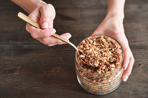 Close-up of unrecognizable woman with natural manicure holding jar and using spoon for muesli