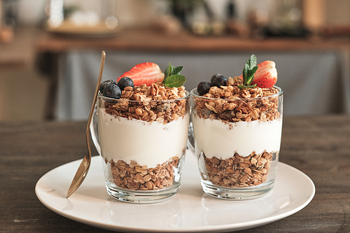 Close-up of two transparent mugs of granola with muesli and summer berries on white plate on dining table