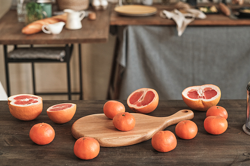 Ripe tangerines and half parts of grapefruits placed on cutting board on wooden table in kitchen