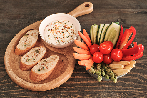 Above view of healthy snacks such as ripe vegetable slices and baguette toasts with spicy sauce on wooden table
