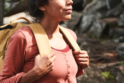 Close-up of content inspired female hiker in pink sweater holding handles of backpack while looking around