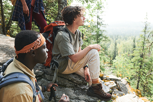 Group of young multi-ethnic hikers being on big stone at mountain and enjoying beauty of nature around them