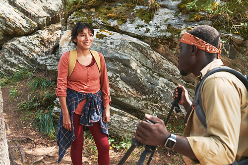 Afro-American man with walking poles talking to smiling mixed race woman standing against rocky mountain