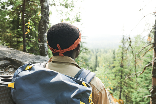 Rear view of Black backpacker with headscarf standing on mountain and looking at forest