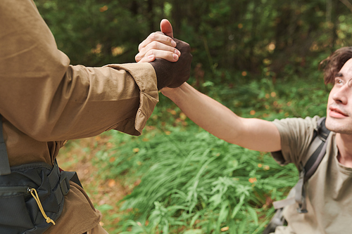 Close-up of black man holding hand of friend while helping him to hike up in forest