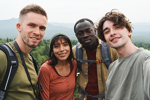 Self-portrait of positive young interracial hikers standing together in mountains during adventure