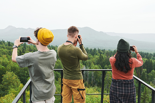 Rear view of hikers standing on bridge and photographing beautiful landscape on devices