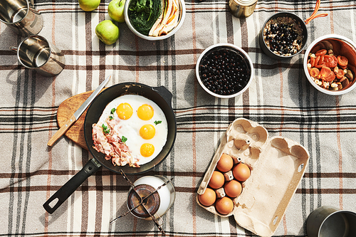 High angle view of fried eggs on pan, thermos mugs, wildberry and burner on checkered plaid outdoors