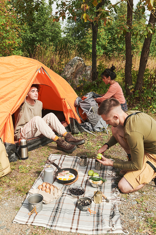 Young hikers unpacking bag and preparing food at lunch halt in forest